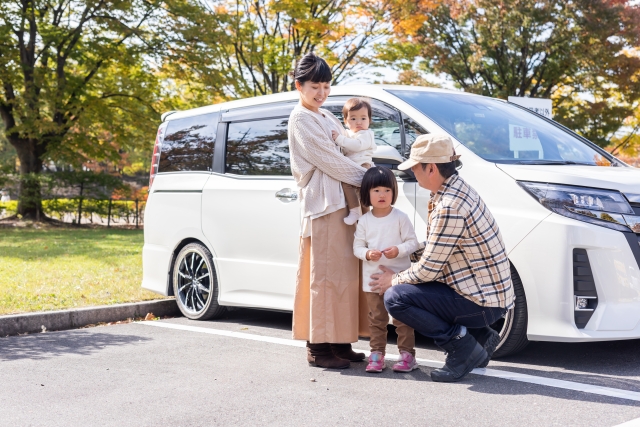 車のそばに立つ赤ちゃんを抱いた家族