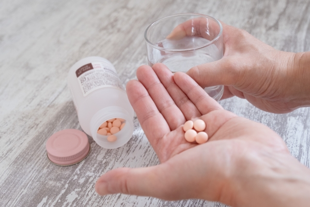 左手の手のひらに錠剤の薬と右手に水の入ったコップ